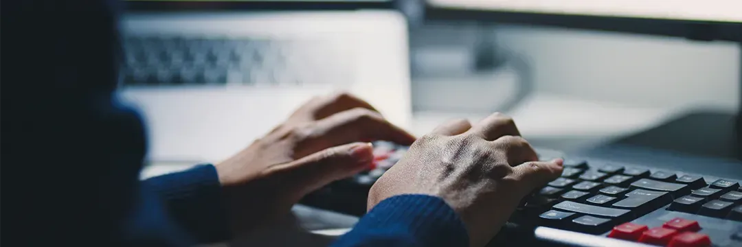 Person skriver på ett tangentbord framför flera skärmar – illustrerar behovet av ID-skydd och hur man skyddar sig mot ID-kapning.