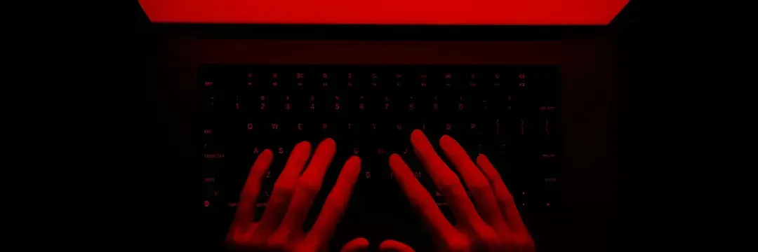 Händer som skriver på tangentbord i rött sken – illustrerar cyberbrott och hur identitetsstöld kan genomföras online.