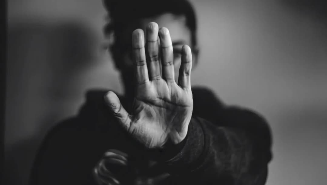 Person i svartvitt håller upp handen framför kameran för att dölja sitt ansikte – symboliserar skyddad identitet och rätten till anonymitet.