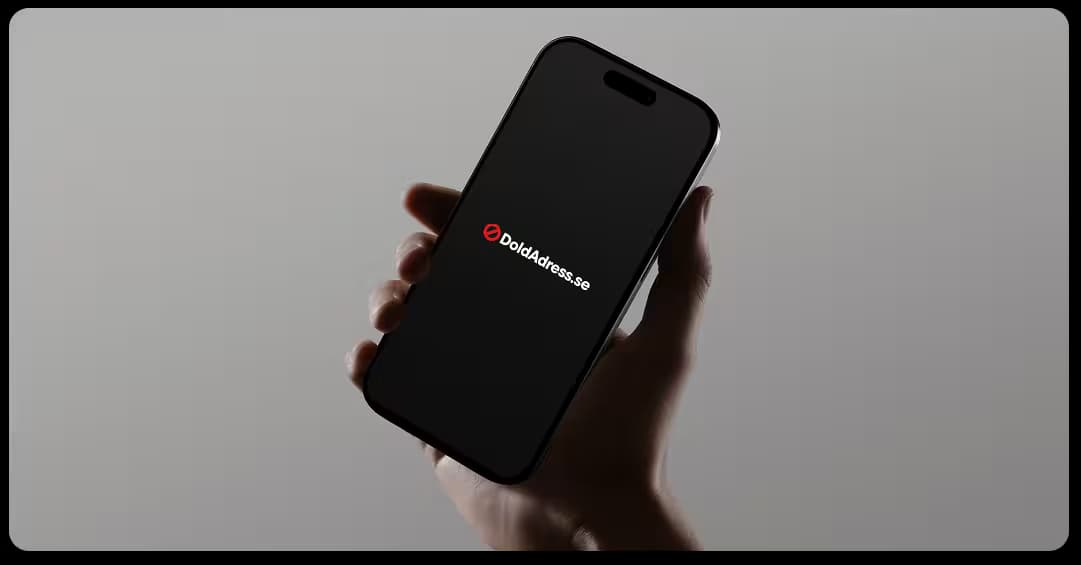Hand som håller i en mobil med svart skärm där DoldAdress.se:s logotyp visas i vitt och rött.